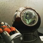 Colour photograph of an early soviet spacesuit next to a spherical descent module