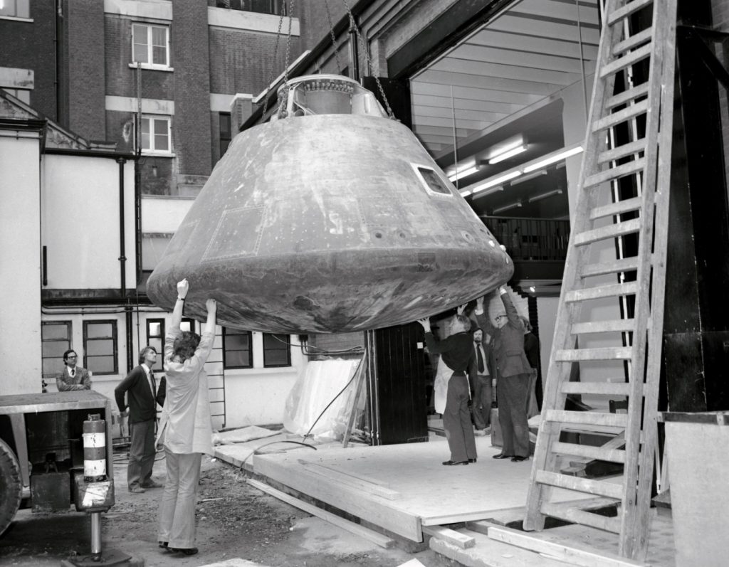 Black and white photograph of the Apollo landing craft being winched into a warehouse at the Science Museum London