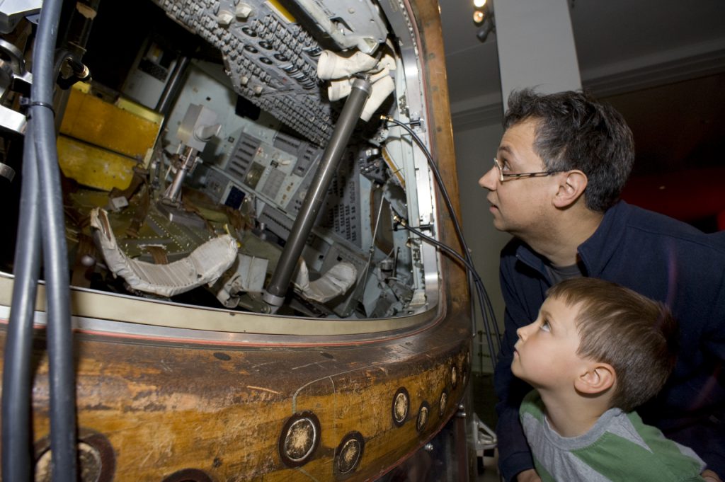 Colour photograph of a man and a boy looking inside the Apollo landing craft on display at the Science Museum London