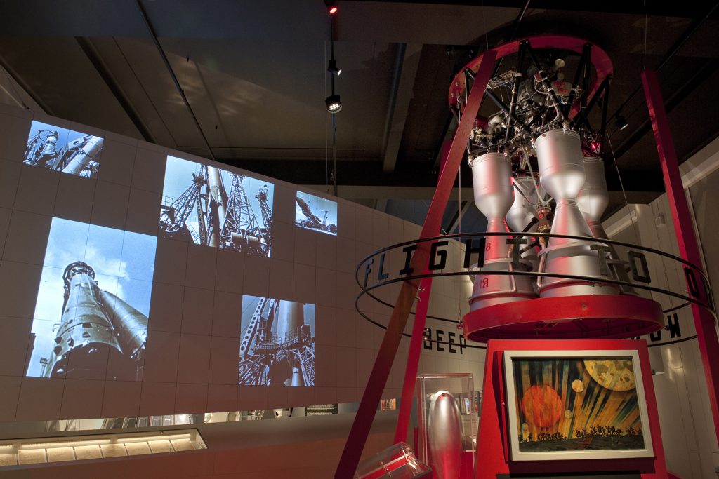 Colour photograph of a section of the Cosmonauts exhibition showing a section of a rocket with images of the rocket projected onto the wall
