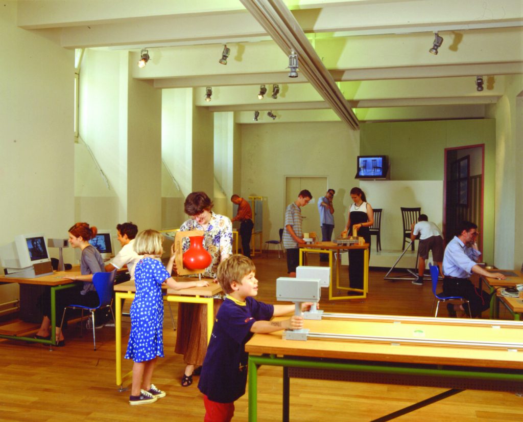 Colour photograph of museum goers using experimentation devices within a museum exhibition