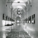 Black and white photograph of a corridor in which are displayed a number of leonardo models paintings and information plaques