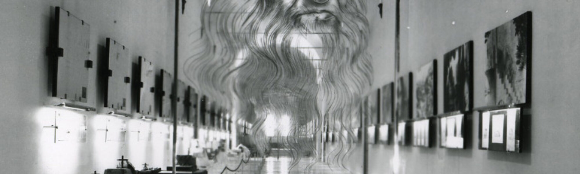 Black and white photograph of a corridor in which are displayed a number of leonardo models paintings and information plaques