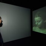Colour photograph of a museum visitor looking at a video projection of a woman sleeping