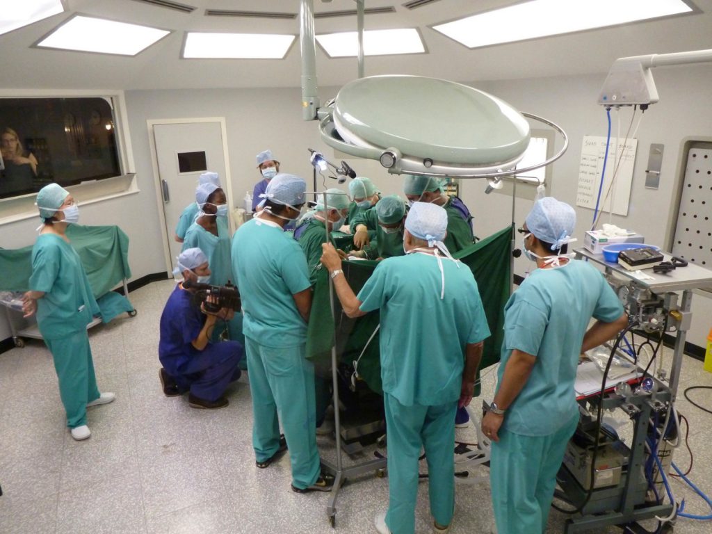 Colour photograph of a simulation based reenactment of a surgical procedure carried out by numerous medical staff