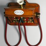 Colour photograph of a wall mounted wooden telephone with two earpieces from the 1880s