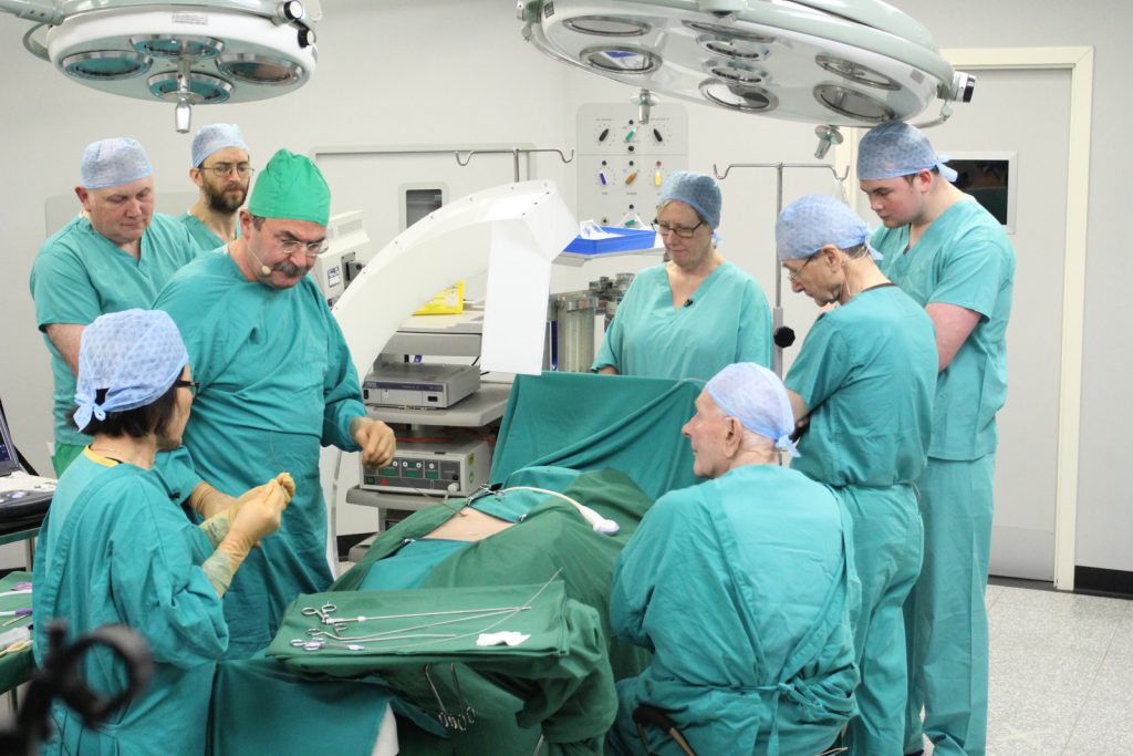 Colour photograph of a simulation based reenactment of a surgical procedure carried out by numerous medical staff
