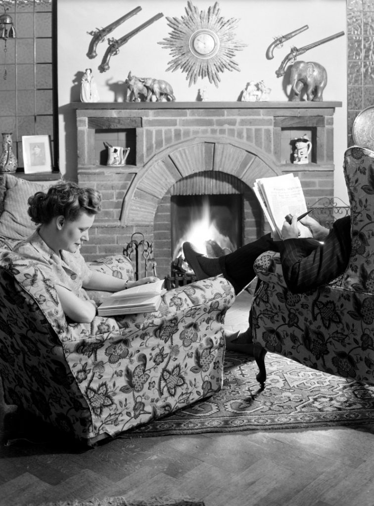 Black and white photograph of a husband and wife sat in front of their living room fire