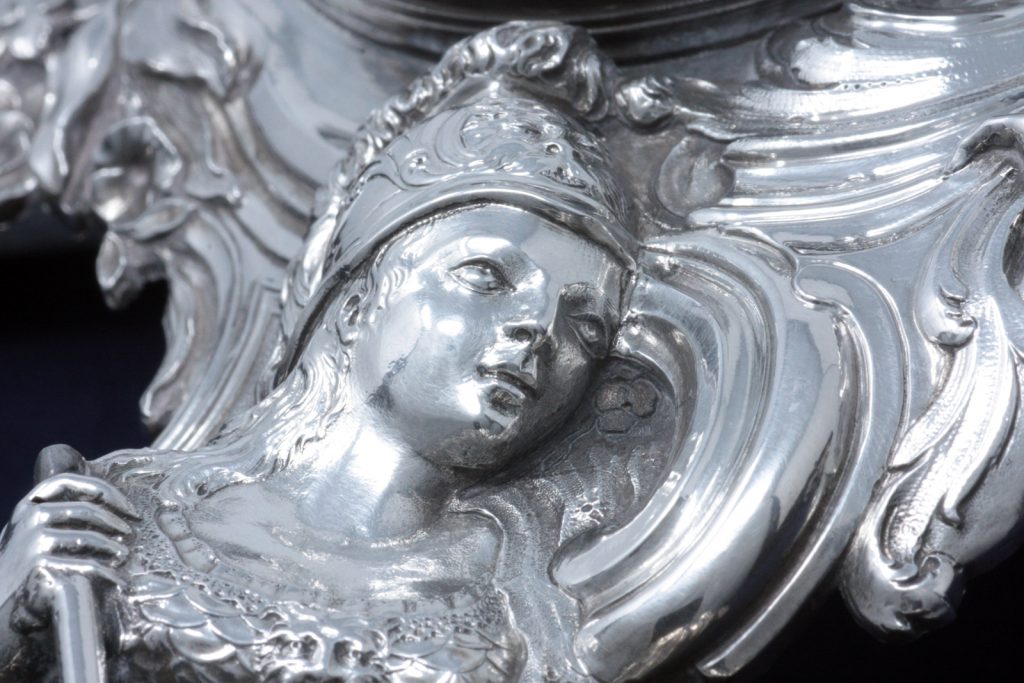 A detail of the silver case of the small clock showing Minerva
