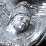 A detail of the silver case of the small clock showing Minerva
