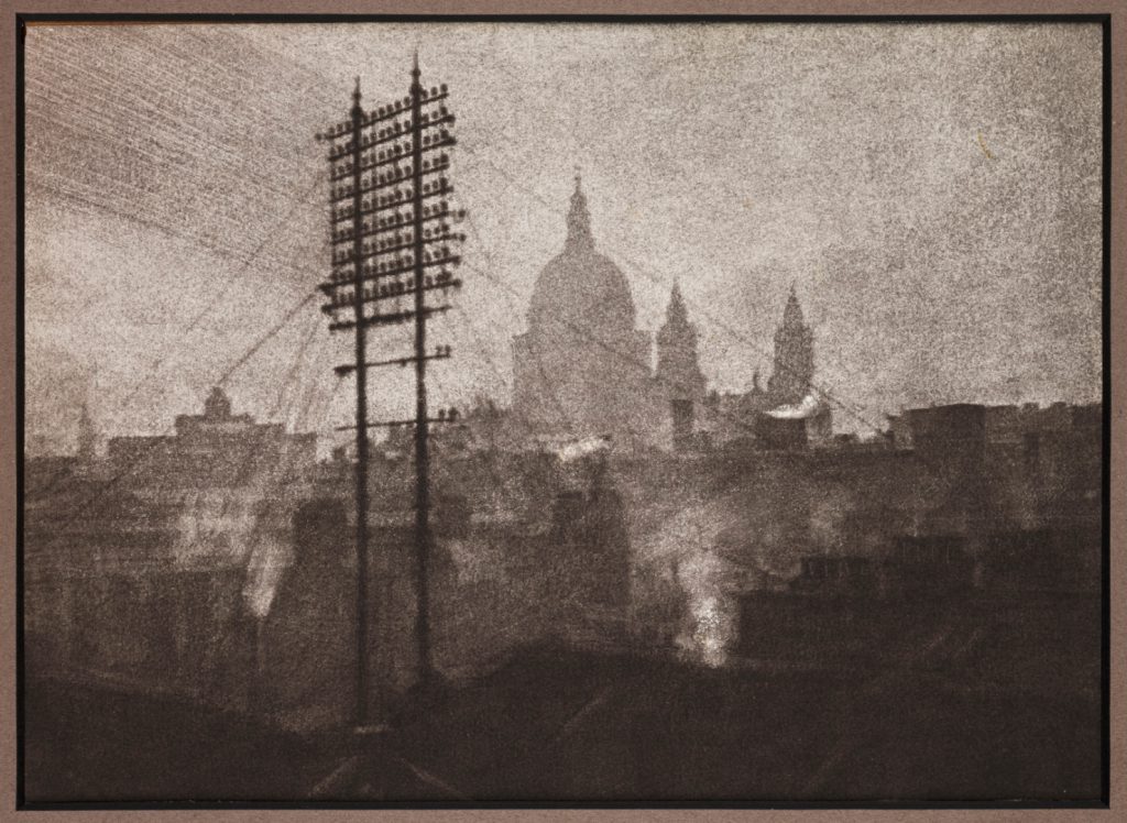 Grainy sepia photograph of a tall telegraph pylon in front of the distant silhouette of Saint Pauls Cathedral