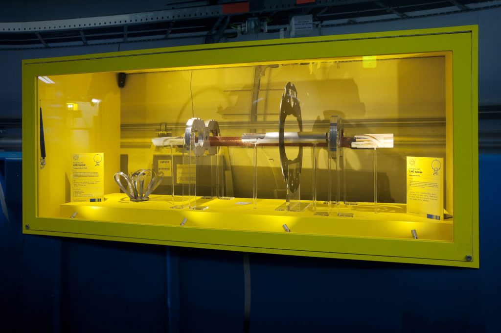 A number of components of an LHC magnet in a yellow display case