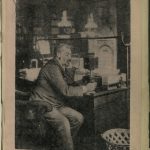 Black and white printed photograph of a man sitting at a desk holding an early table telephone from 1891