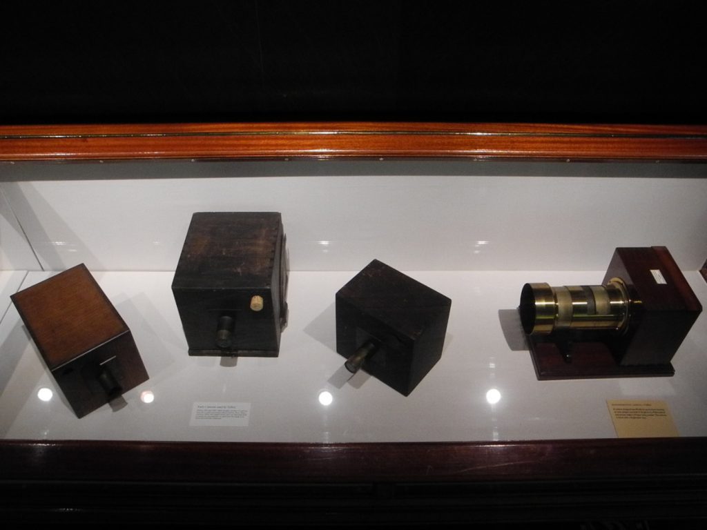 Colour photograph of four early wooden box cameras on display in a glass case