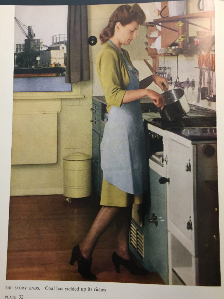 Page in a magazine showing a colour photograph of a woman cooking over a stove. The caption reads coal has yielded up its riches