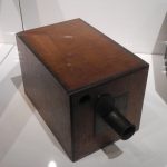 Colour photograph of an early wooden box camera on display in a glass case