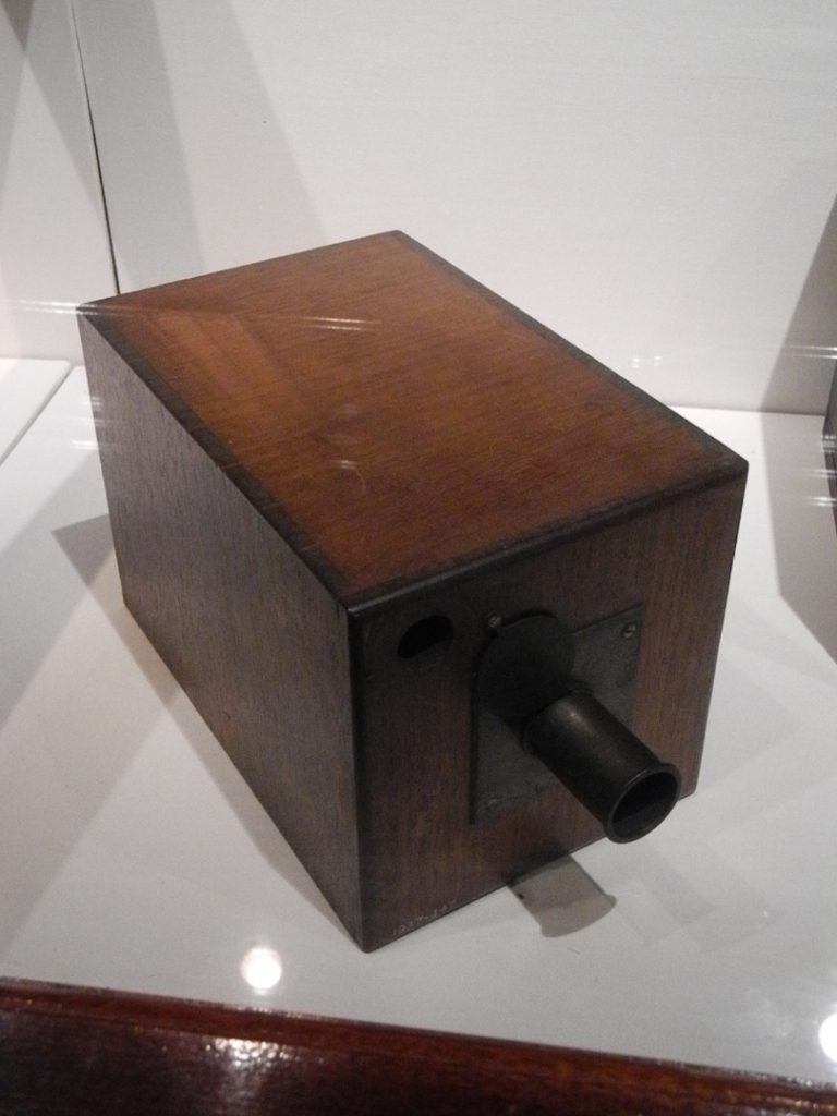 Colour photograph of an early wooden box camera on display in a glass case