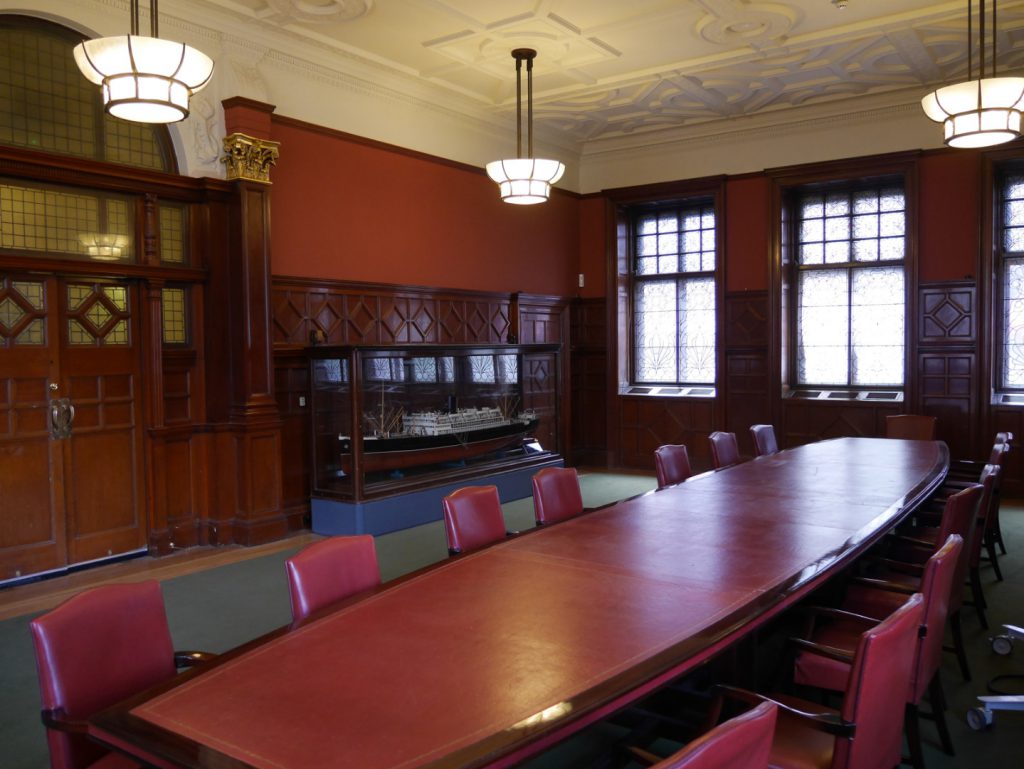 Colour photograph of a long leather topped meeting table with a glass case contained ship model behind