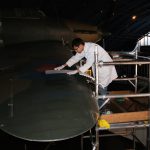 Colour photograph of a conservator repairing a tear on the wing of a Hawker Hurricane aircraft