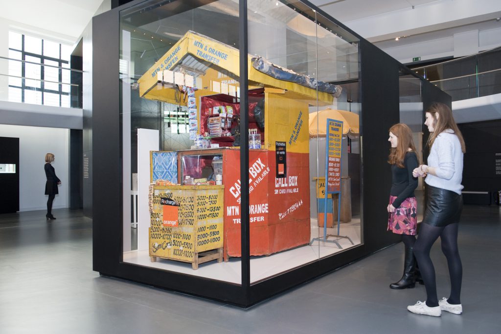 Colour photograph of the connecting Africa display in Information Age showing visitors viewing a mobile phone repair hut from Cameroon