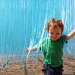 A toddler runs through a suspended collection of blue plastic strings