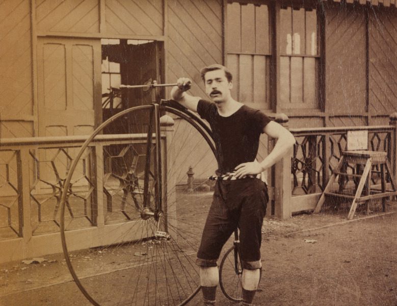 Sepia photograph of a cyclist with his high wheeler bicycle from the late nineteenth century