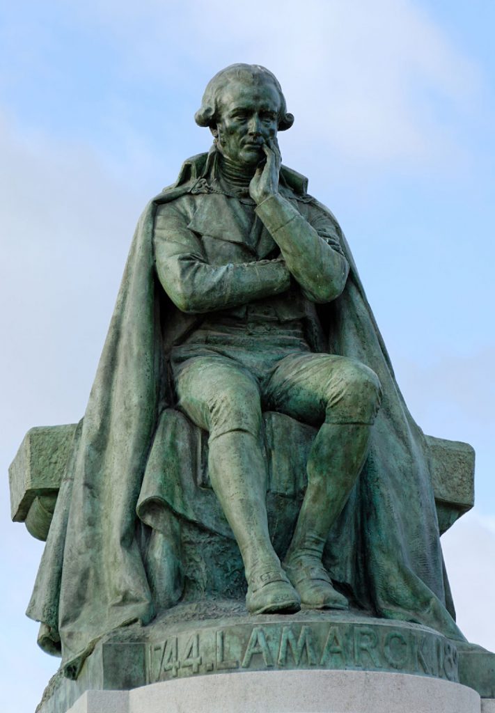 Metallic statue of Jean-Baptiste Lamarck in a sitting pose atop a stone pedestal