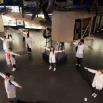Several members of the National Youth Theatre stand with arms outstretched in the Flight Gallery at the Science Museum