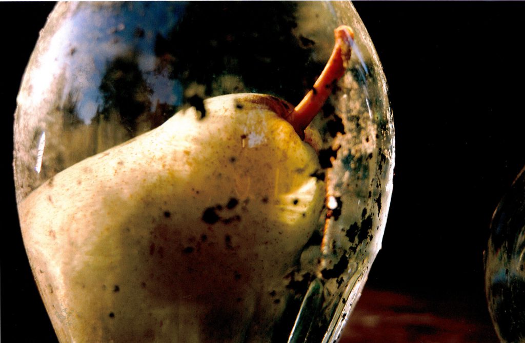 Still image from a colour video showing a pear sitting within a glass container