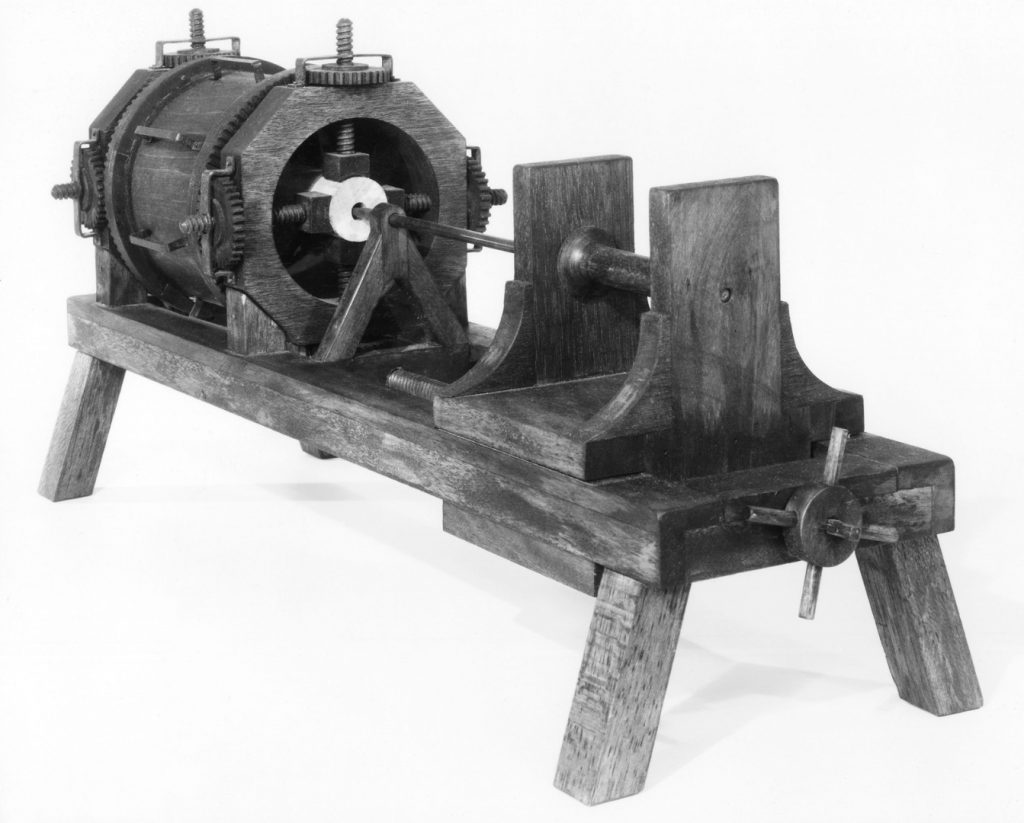 Black and white photograph of a working model of a wooden machine for boring holes in wood
