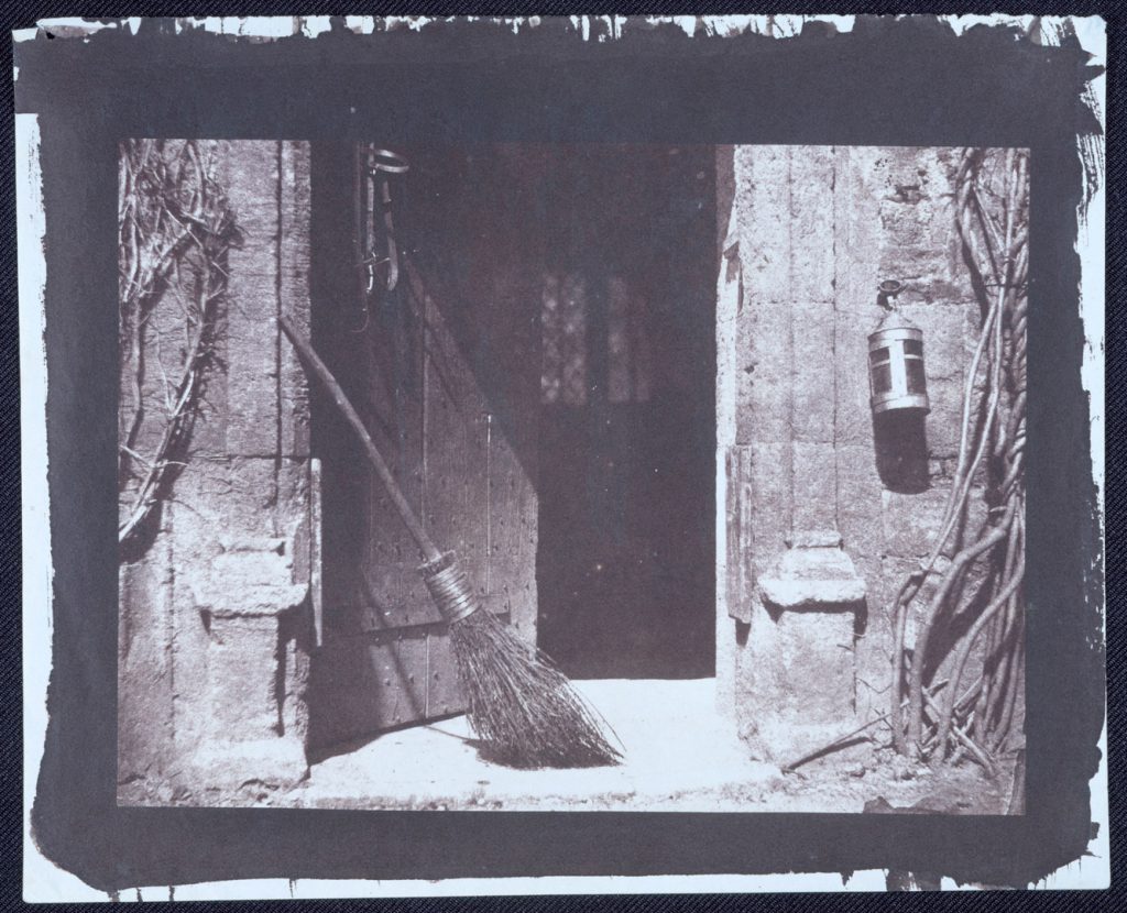 Early black and white photograph by William Henry Fox Talbot of an open door with broom and lantern