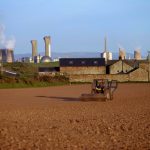 Colour photograph of a field being ploughed with a nuclear power station in the background