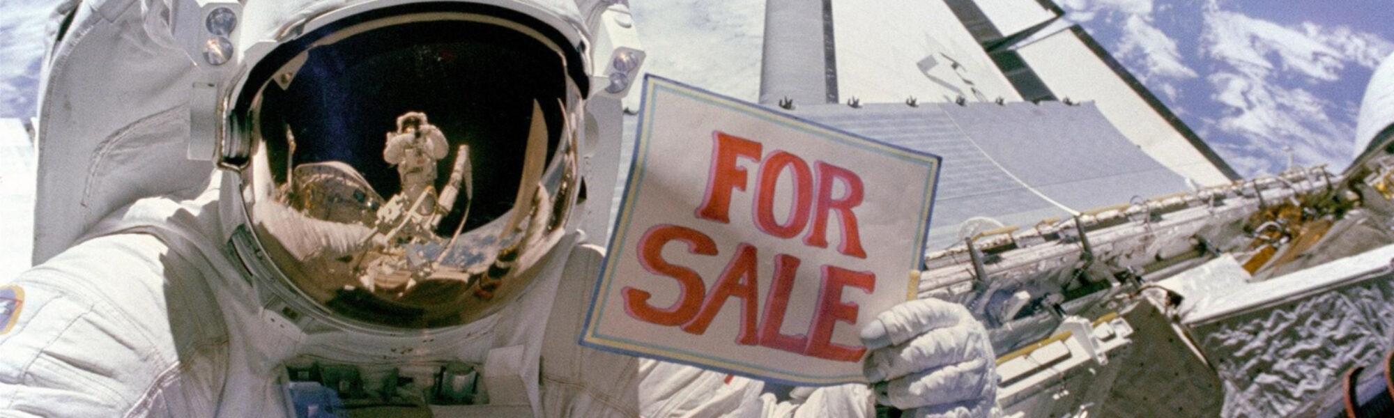 Colour photograph of an astronaut in space floating above a spacecraft and holding up a sign which reads for sale