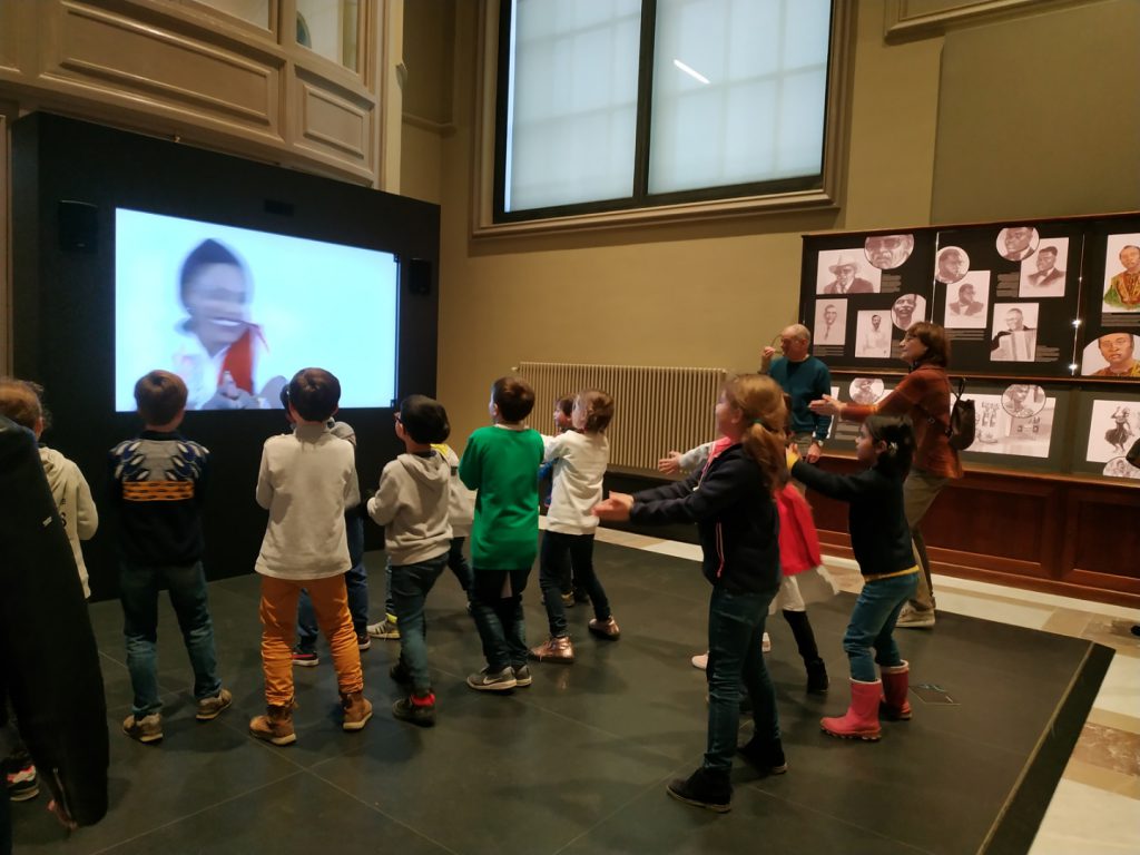 Colour photograph of children copying a dance from a screen in a museum gallery