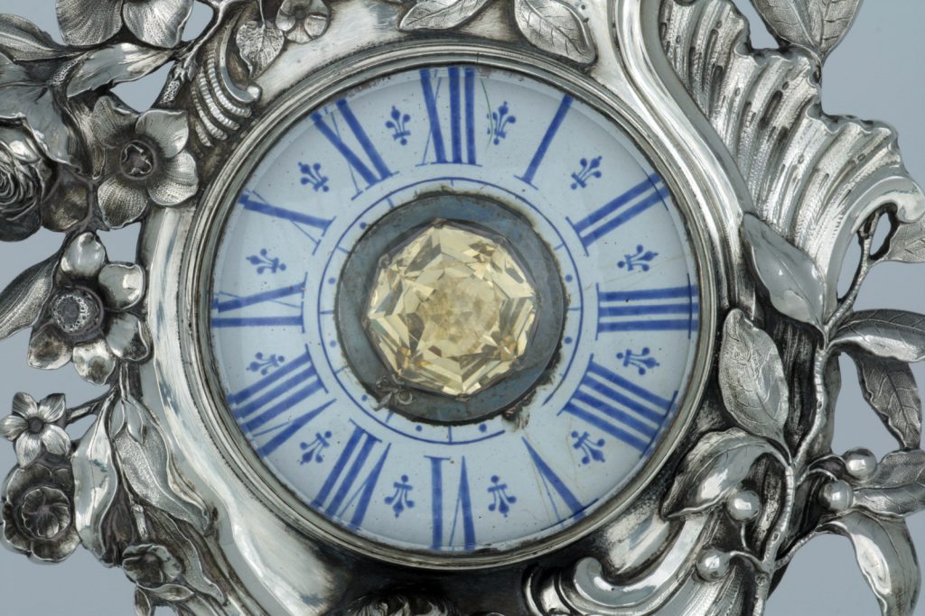 A photograph showing a detail of the clock with a large central citrine quartz jewel