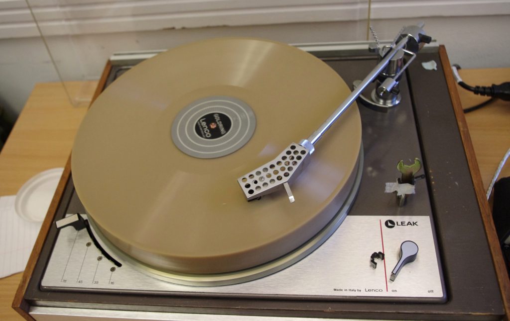 Colour photograph of a freshly recorded wax disc playing on a transcription turntable