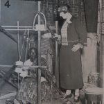 Black and white photograph of a Nigerian worker seated and a loom and European woman observing