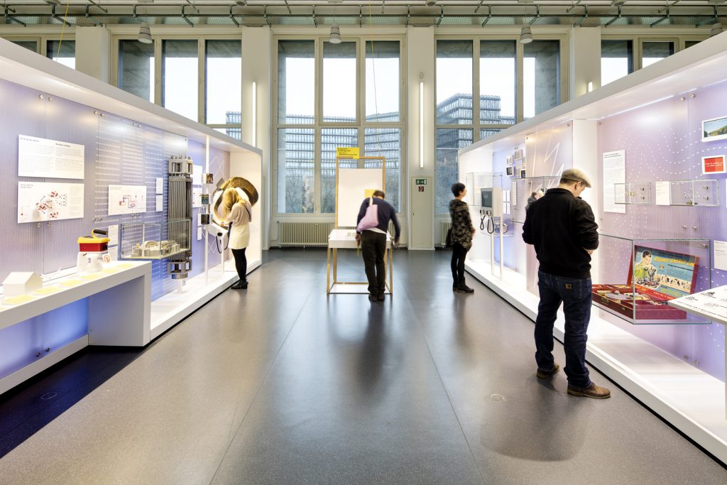 Colour photograph of a bright exhibition space with display objects and visitors
