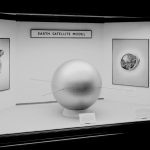 Black and white photograph of a model of an early satellite on display as part of an exhibition