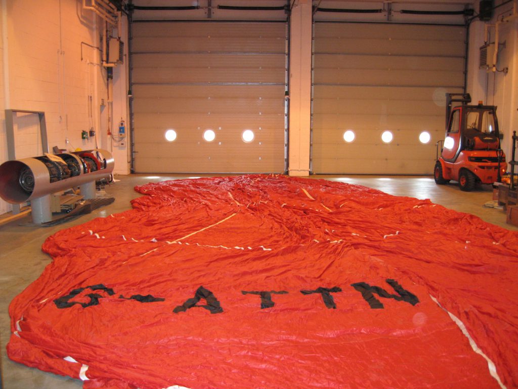 Colour photograph of a large deflated hot air balloon canvas spread on the floor of a warehouse