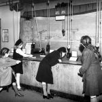 Black and white photograph of schoolgirls lifting weights using pulleys at a museum exhibition