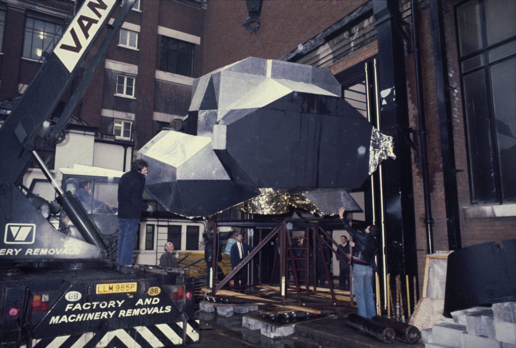 Colour photograph of a moon landing unit being winched into a warehouse at the Science Museum London