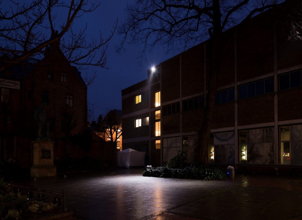 Colour photograph of a building and courtyard lit sparsely by a spotlight