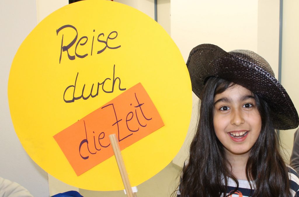A girl in a hat holds a banner saying 'reise durch die zeit' meaning 'Journey through time'