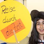 A girl in a hat holds a banner saying 'reise durch die zeit' meaning 'Journey through time'