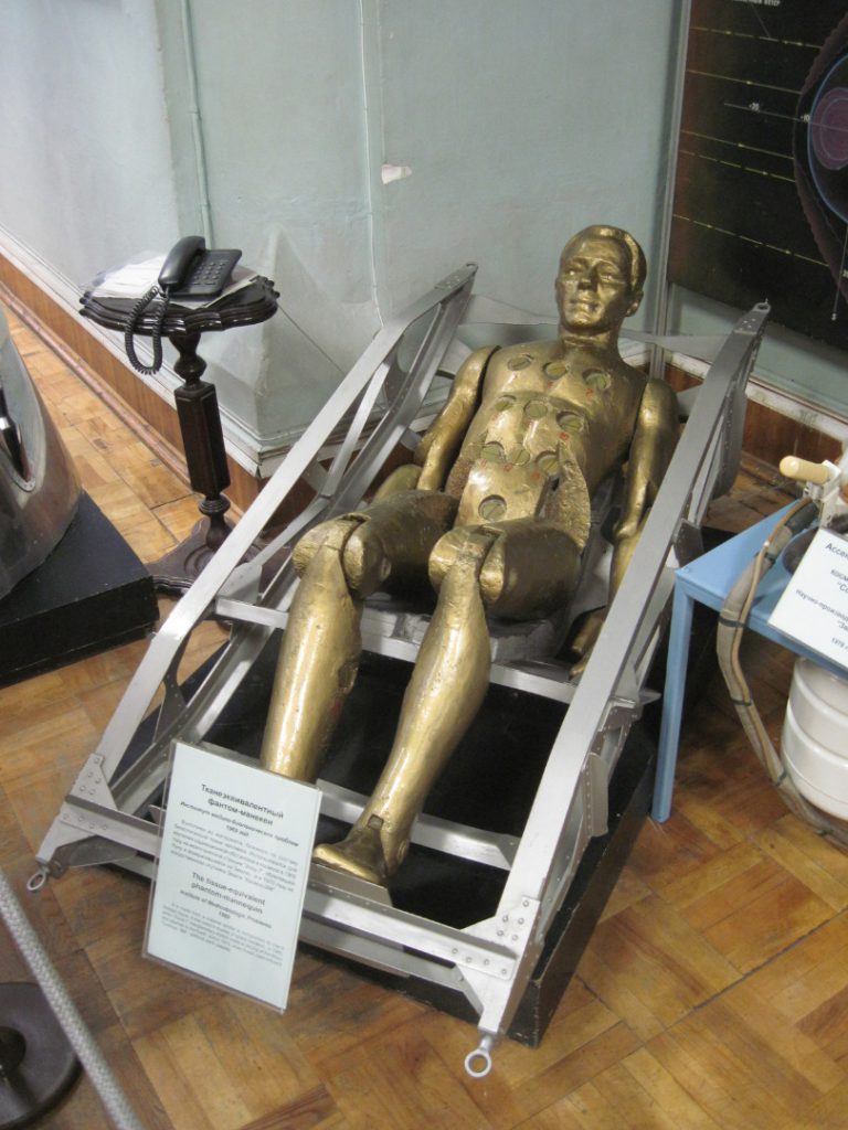 Colour photograph of a gold coloured mannequin lying inside a space craft pilot seat