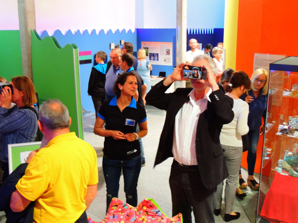 Colour photograph of museum goers using hand held viewing devices within an exhibition of colour