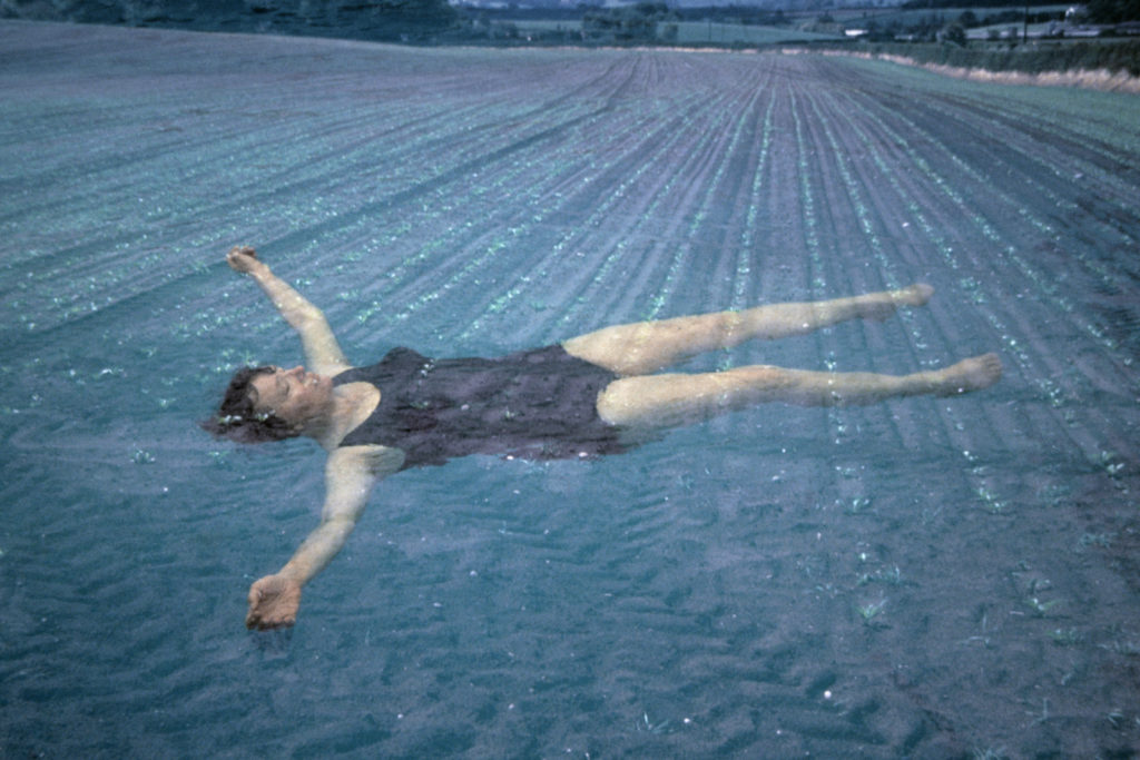 Video still depicting a woman floating in the soil of a ploughed field