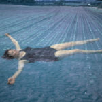 Video still depicting a woman floating in the soil of a ploughed field
