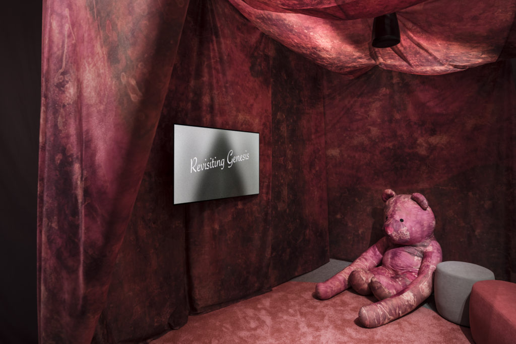 Colour photograph of a video showing in an exhibition room with a large pink teddy bear